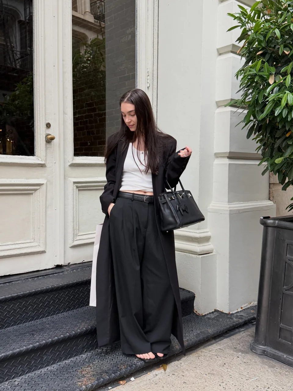 Diana on steps in a black blazer and wide-leg trousers with a white cropped top, carrying a black handbag