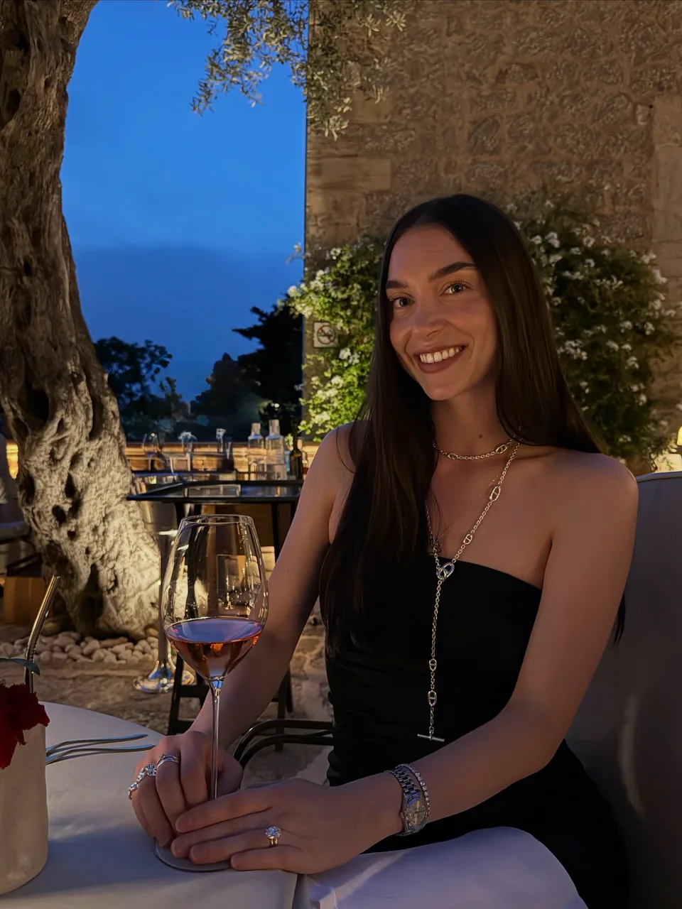 Diana seated outdoors at dusk in a black strapless dress